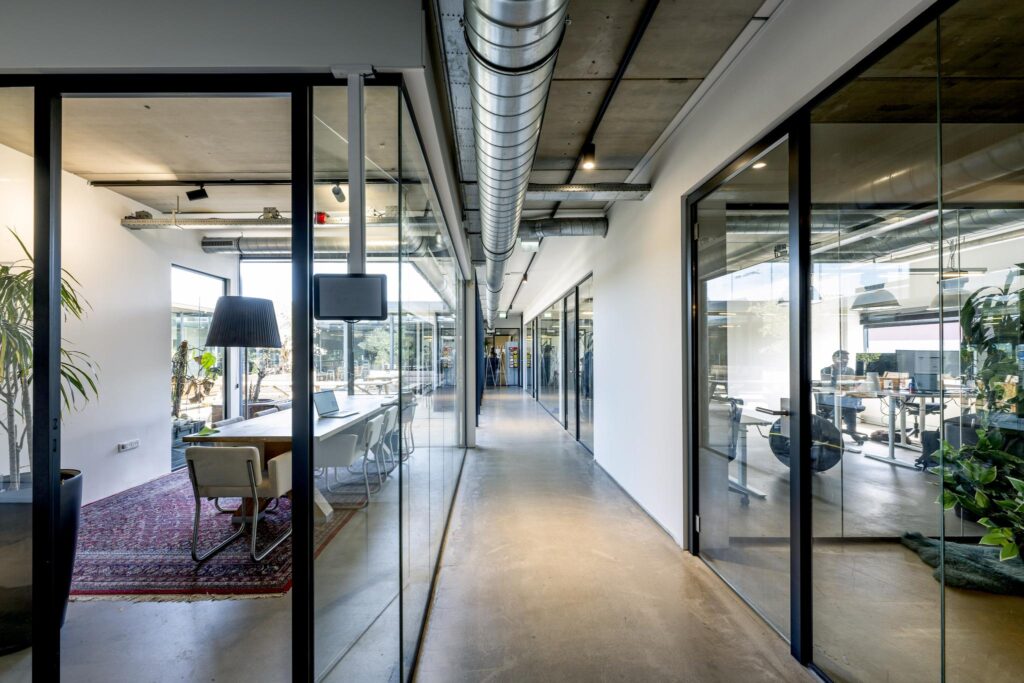 Modern office hallway on Johan van Hasseltweg with glass-walled meeting rooms and industrial ceiling design.